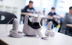 Un casque de réalité virtuel est posé sur une table. On distingue des enfants à l'arrière-plan.
